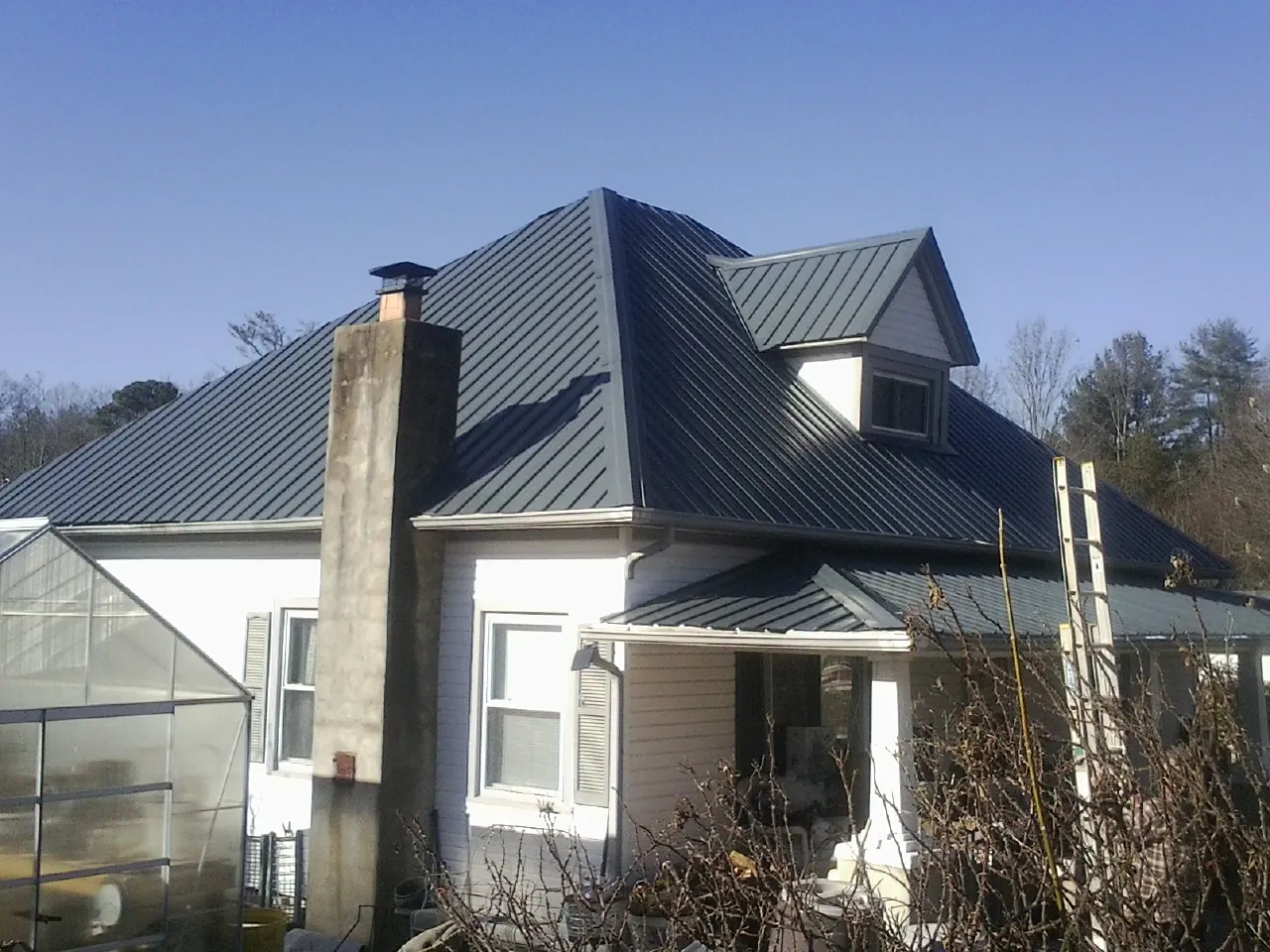 Dark blue standing seam metal roof on a white farmhouse with dormer — Slate & Tile Roof Repair by Roofing Brothers in Moville