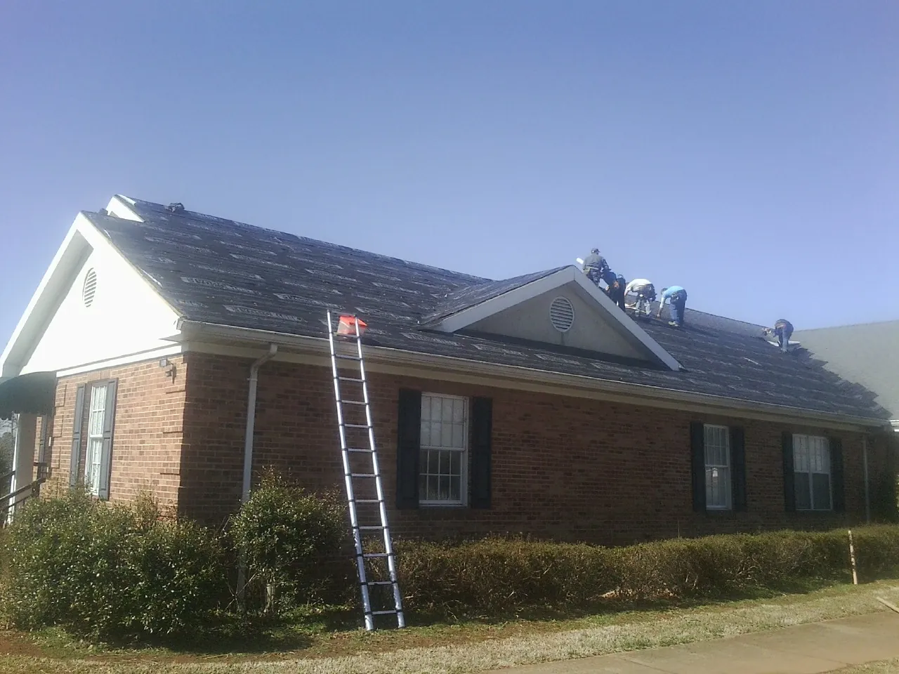 Crew tearing shingles off a brick ranch roof with a ladder set — Emergency Roof Repair work by our crew in Moville