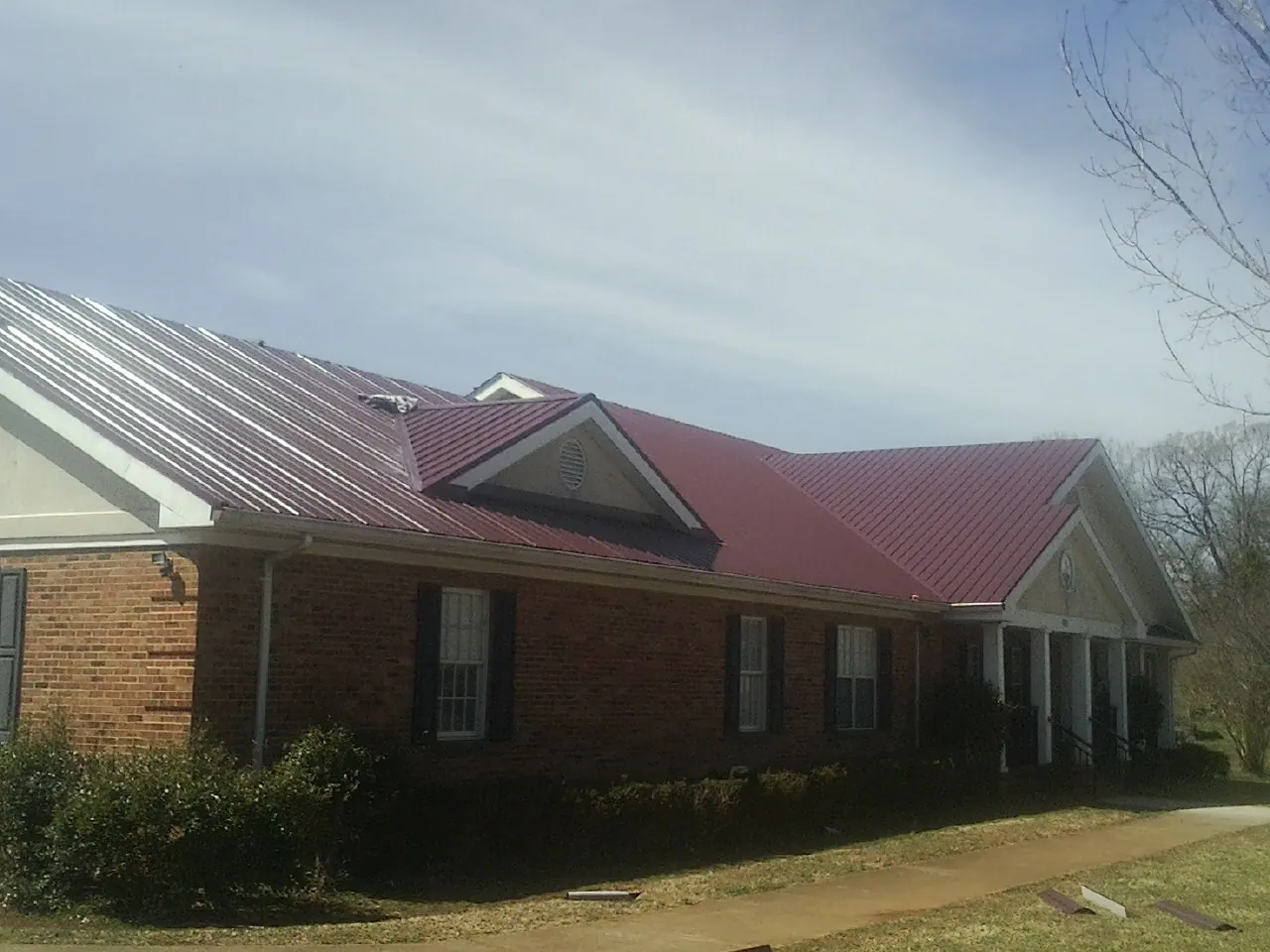 Red metal roof with gabled entries on a long brick building, from a Hail Damage Roof Repair job in Moville