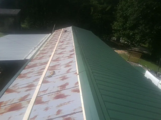 Old rusted panels beside newly installed green metal roofing — Wind Damage Roof Repair by Roofing Brothers in Moville