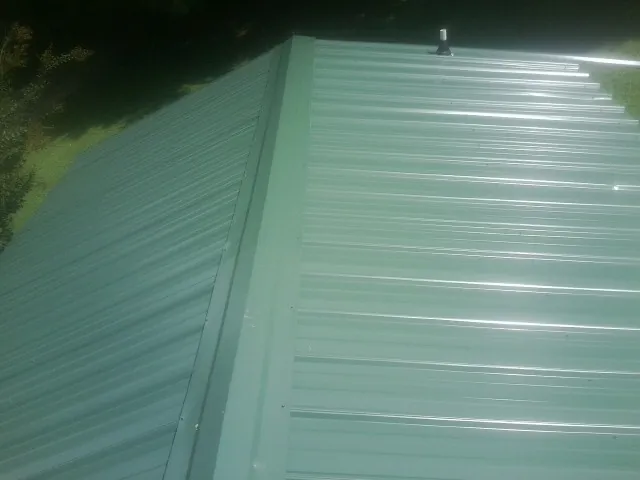 New green metal panels meeting at the ridge of a roof — Flat Roof Repair work by our crew in Moville