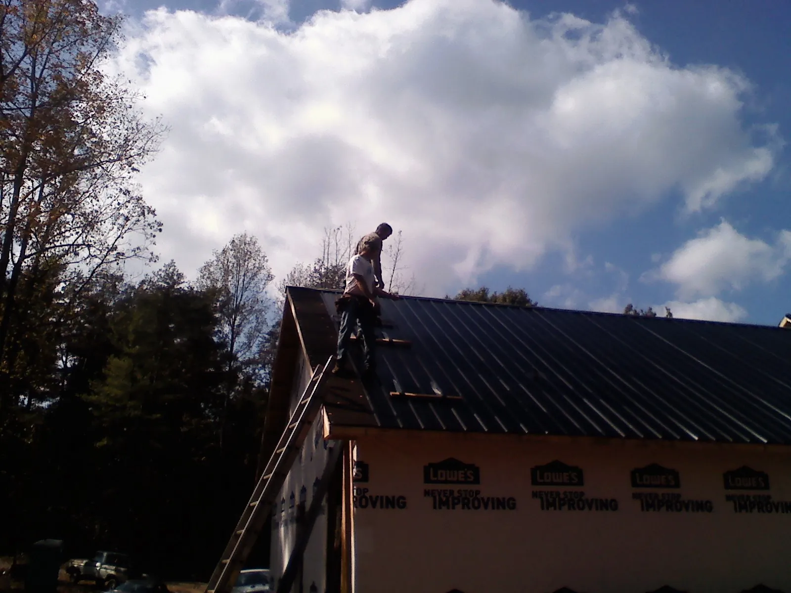 Roofer fastening dark metal panels high against a cloudy sky, from a Roof Inspection job in Moville