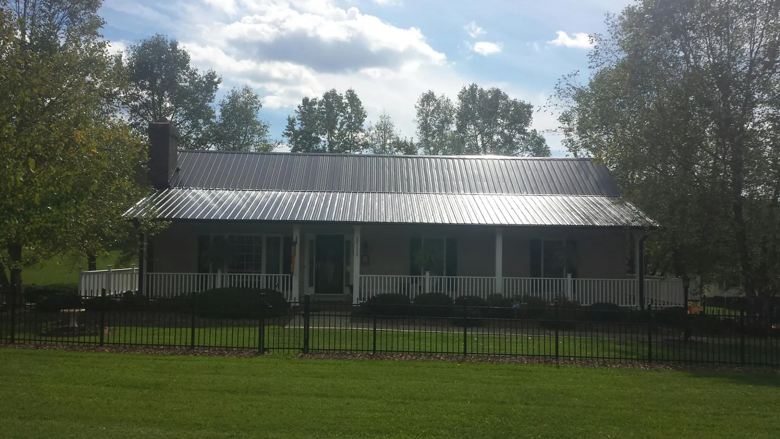 Gray metal roof on a brick ranch with a full width front porch — Gutter Guard Installation work by our crew in Moville