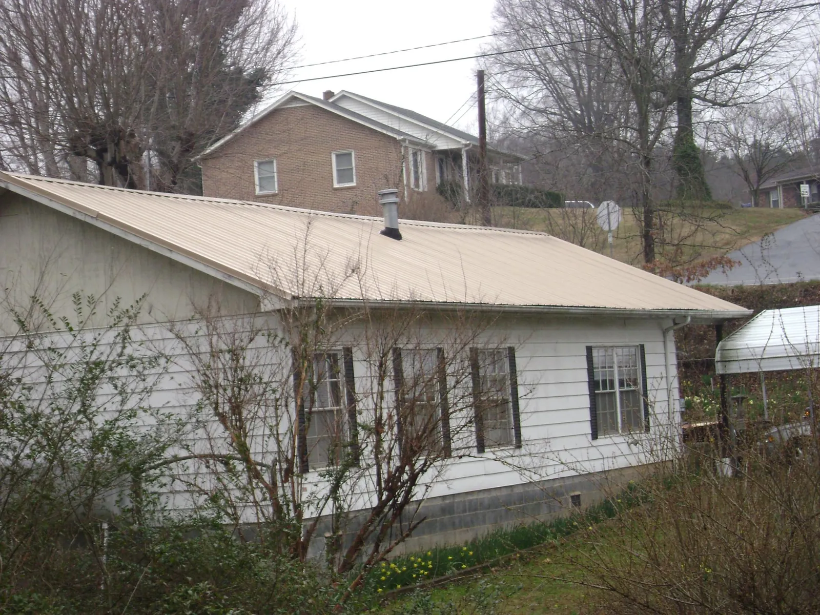 Tan metal roof on a white sided house set into a hillside — Commercial Roofing by Roofing Brothers in Moville