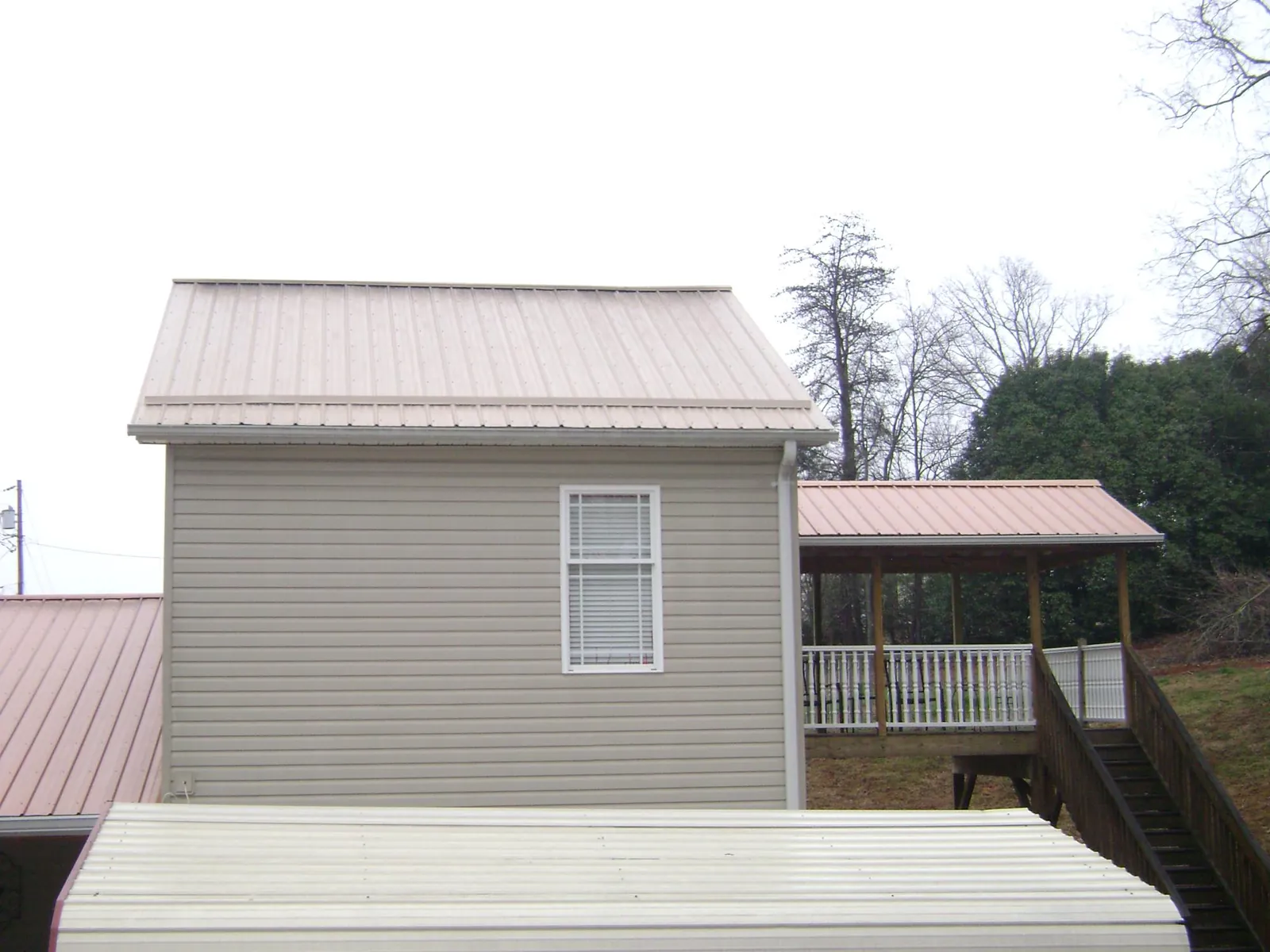 Tan metal roofs on a two story addition and attached porch, from a Roof Replacement job in Moville
